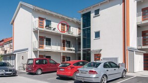 Un edificio de varios pisos con un estacionamiento. Hay tres coches aparcados al frente.