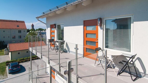 Un edificio moderno con balcón, barandillas de vidrio y un automóvil estacionado cerca.