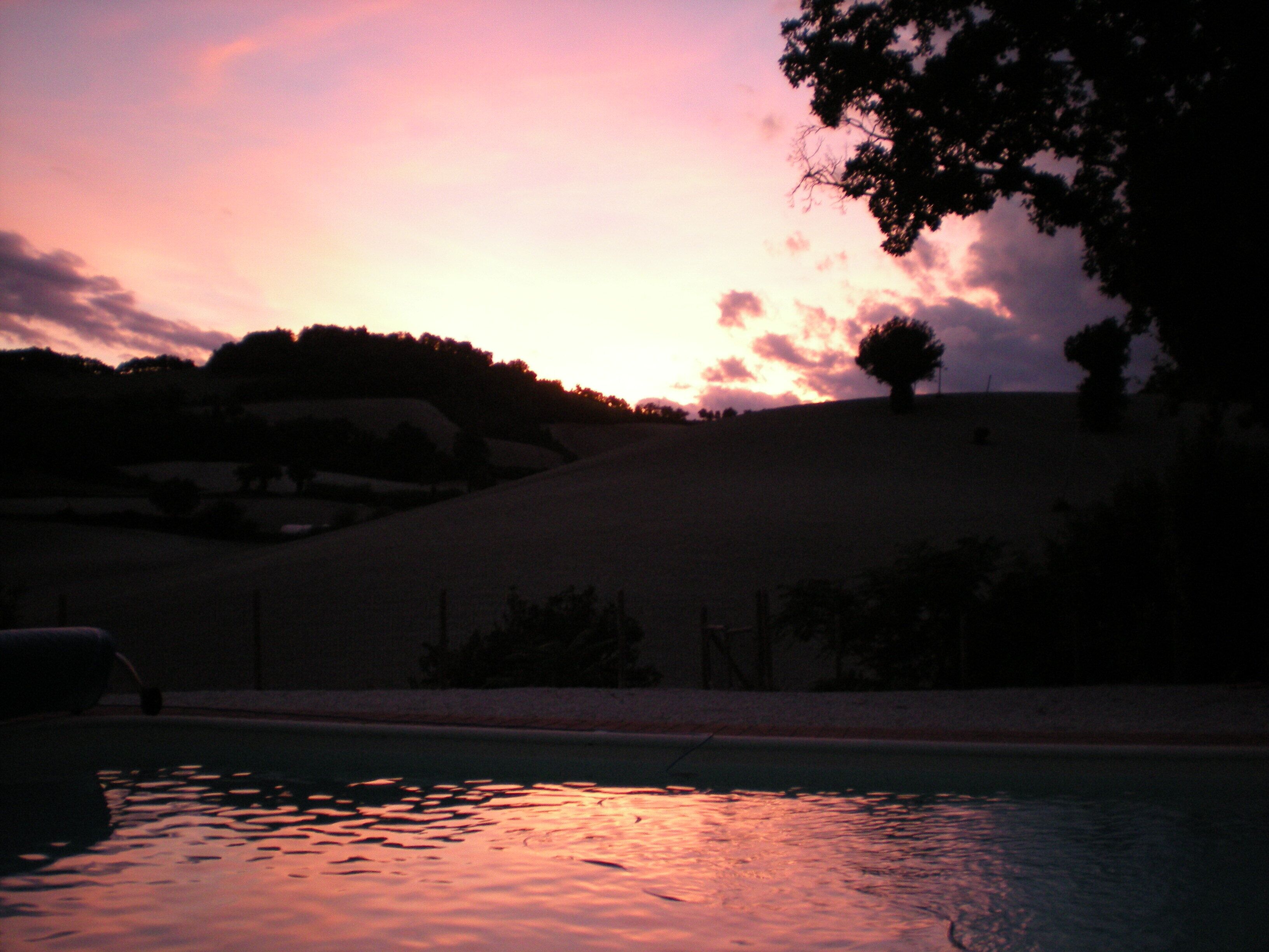 Un atardecer sobre un cuerpo de agua con la silueta de una colina y árboles al fondo.