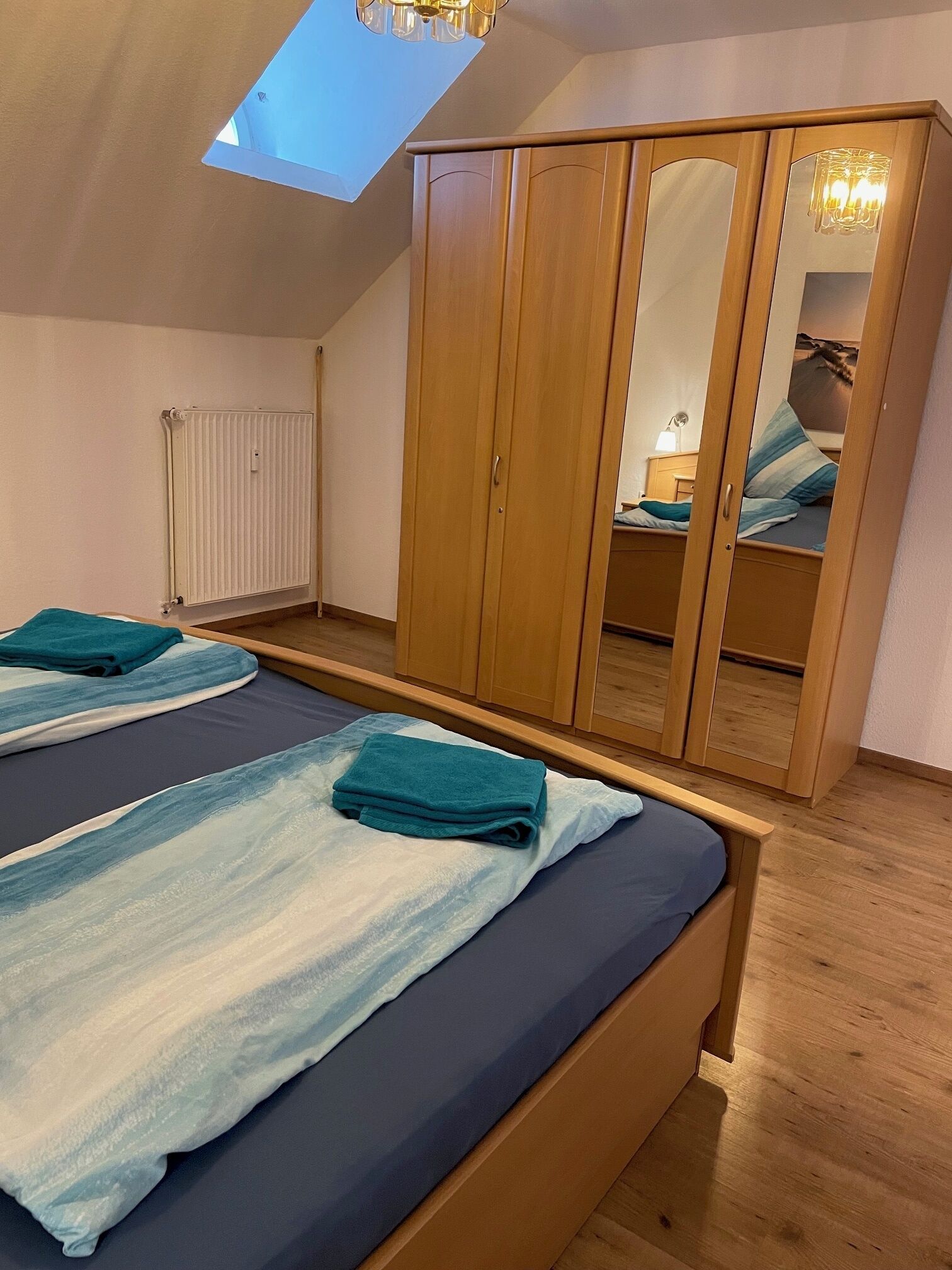 A bedroom with two beds, wooden wardrobe, and a skylight.