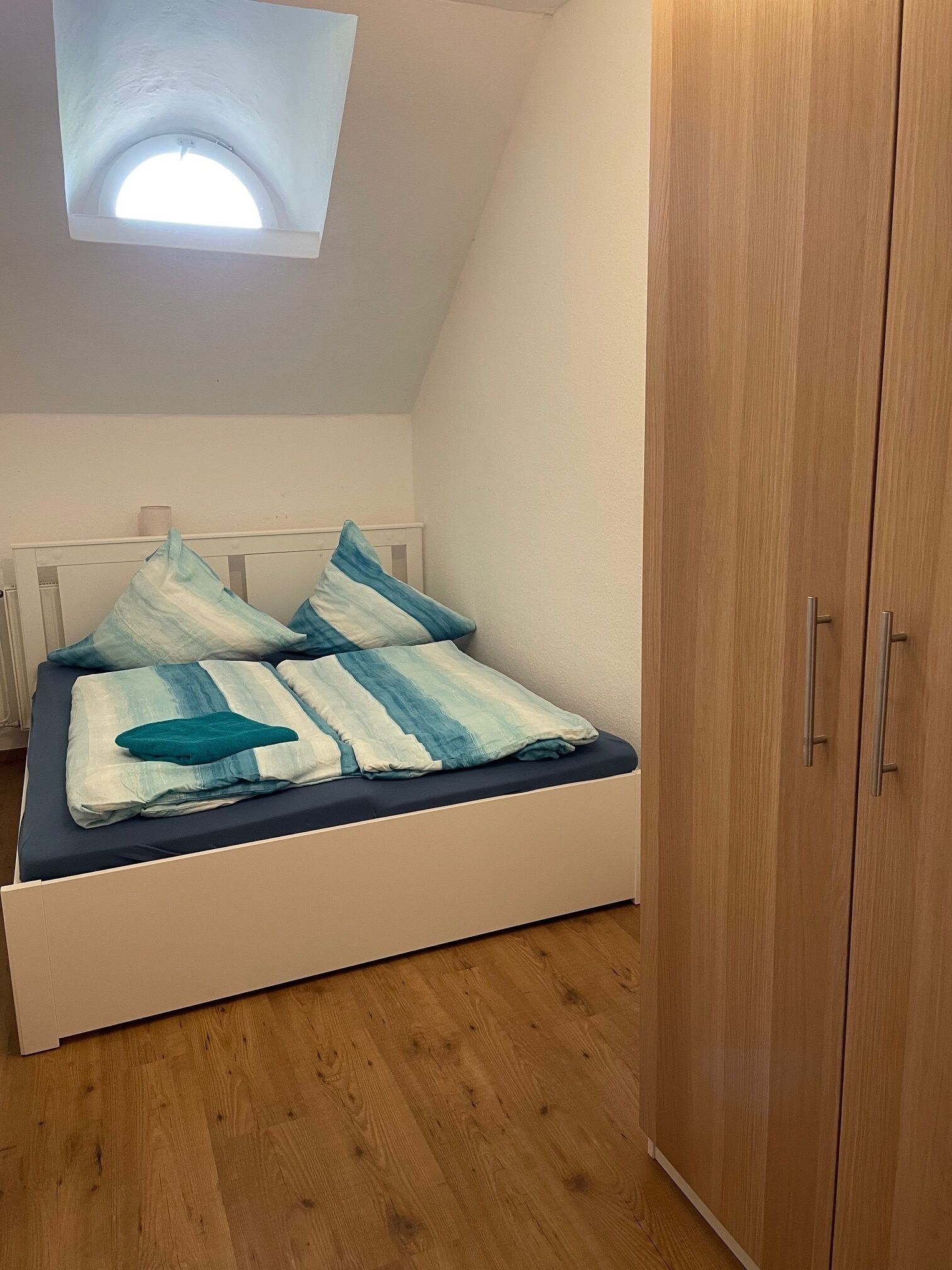 Una camera da letto con un lucernario, un letto con biancheria azzurra e bianca, e pavimento in legno.
