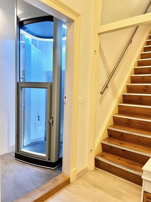 Un intérieur moderne avec un ascenseur en verre, un escalier en bois et un sol carrelé.