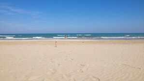 Une plage avec un ciel dégagé, une personne dans l’eau et des empreintes de pas sur le sable.