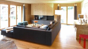 Un salon spacieux avec un grand canapé noir, un plancher en bois et une cheminée.