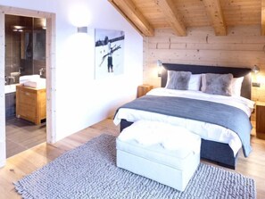 A bedroom with a bed, bedside tables, a nightstand, a wooden bench, and a bathroom with a mirror and sink.