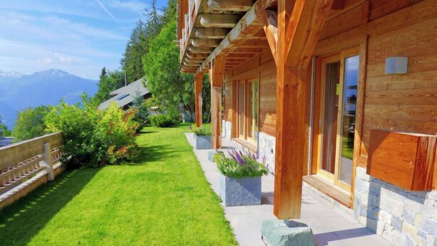 Une cabane en bois avec des fondations en pierre, une pelouse bien entretenue et une vue sur les montagnes en arrière-plan.