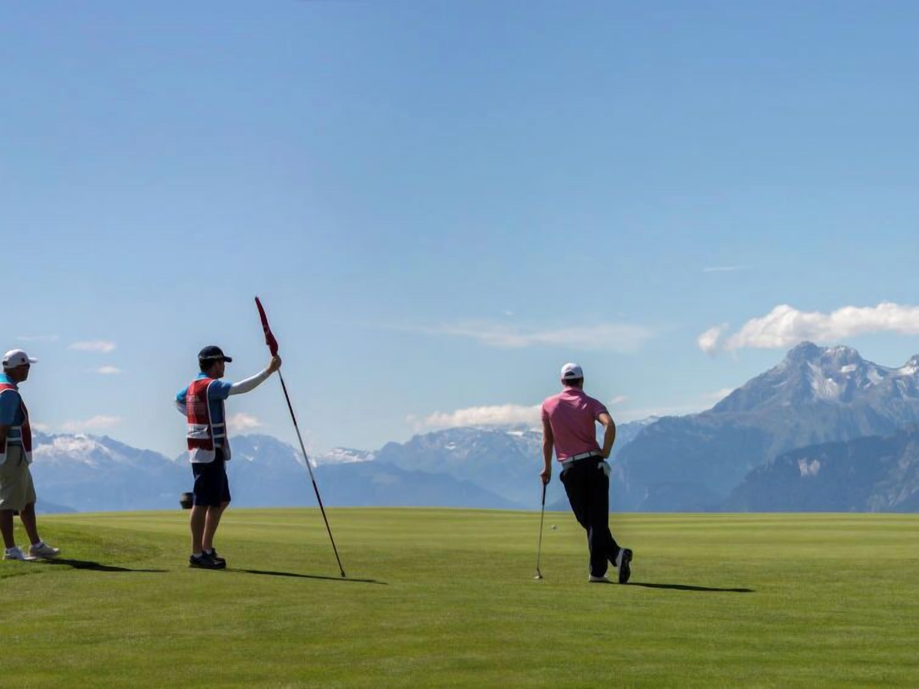Un terrain de golf où l’on voit des joueurs en action, un ciel dégagé et des montagnes en arrière-plan.