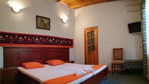 A bedroom with a wooden bed, two bedside tables, a wooden door, a chair, and a television on the wall. - Hostel&Guesthouse Sim Sim (Samarkand)