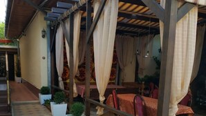 A covered outdoor seating area with hexagonal tiled flooring, white planters with small trees, and red cushioned chairs. - Hostel&Guesthouse Sim Sim (Samarkand)