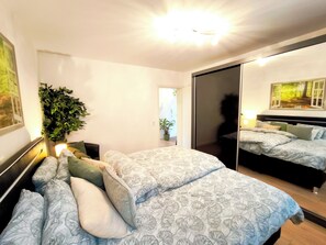 Un dormitorio con una cama, un espejo, una planta en maceta y una puerta que da a otra habitación.