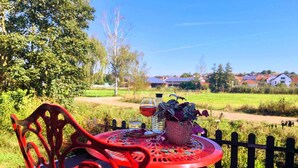 Un juego de mesa y sillas de metal rojo sobre una terraza de madera con vista a un paisaje rural.