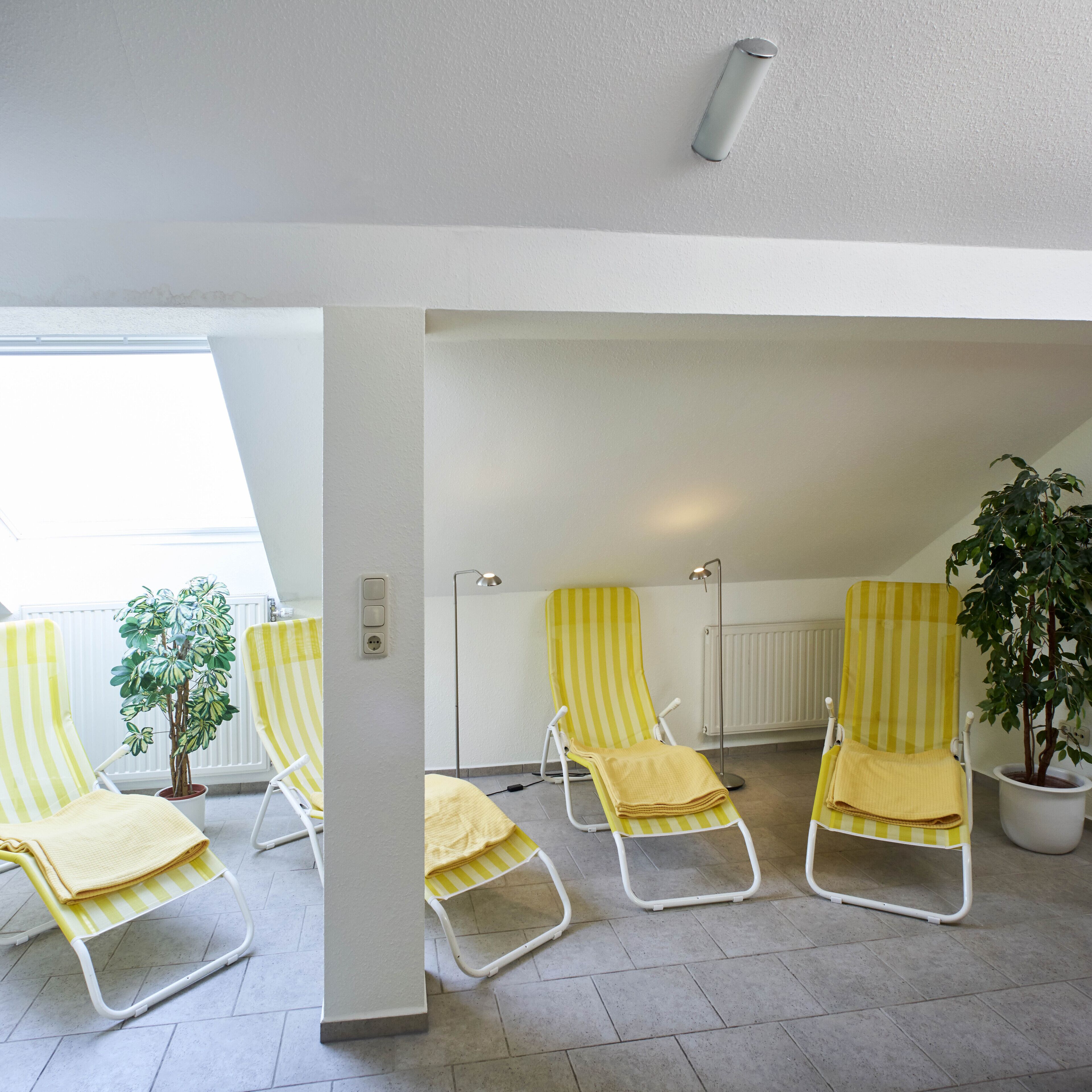 A room with three yellow-striped lounge chairs, a potted plant, and a radiator.