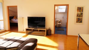 A modern living room with a flat-screen TV, wooden flooring, and a large window providing natural light. - Refuge with a wonderful view (MERAN)