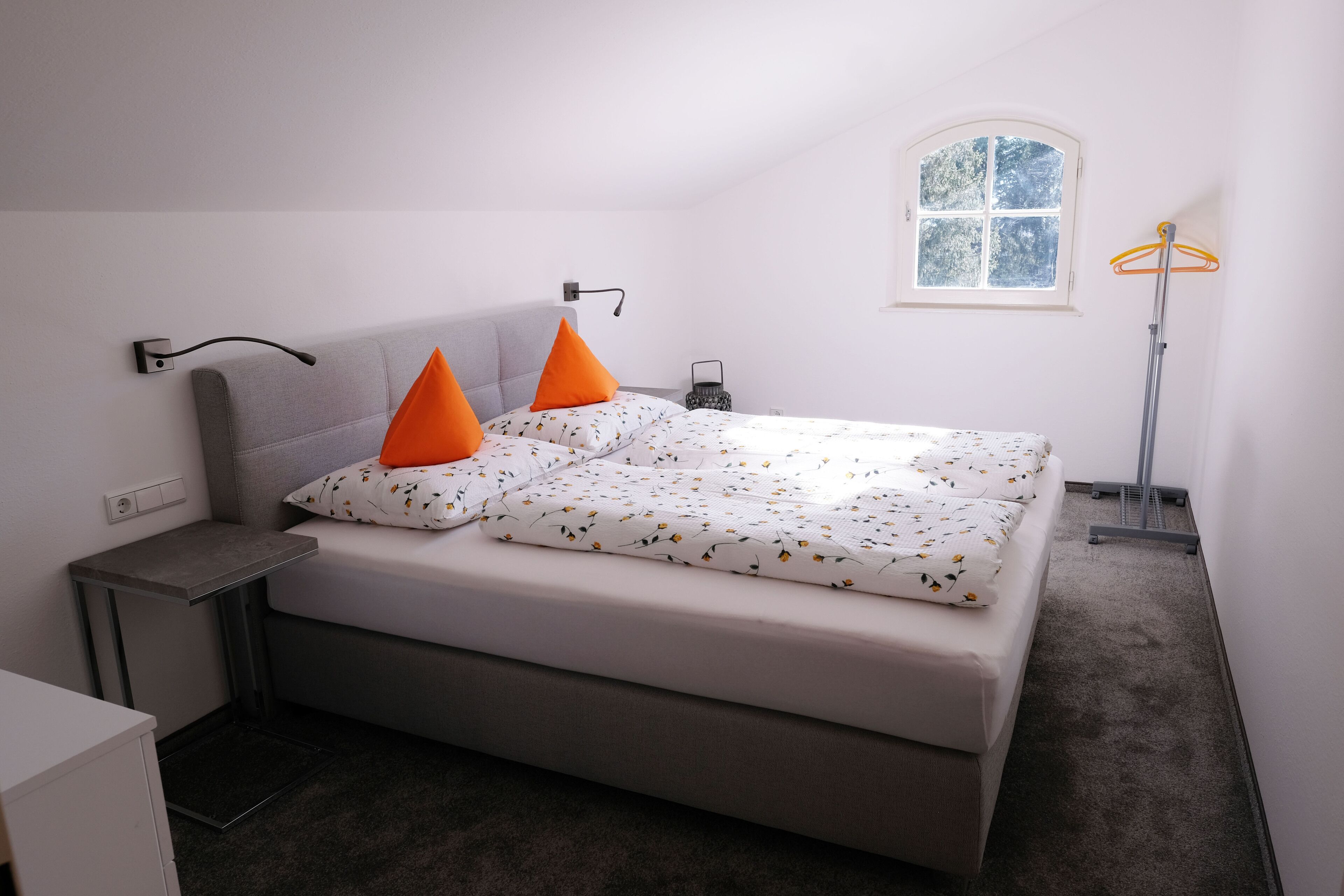 A bedroom with a bed, a nightstand, a lamp, a window, and a floor lamp.