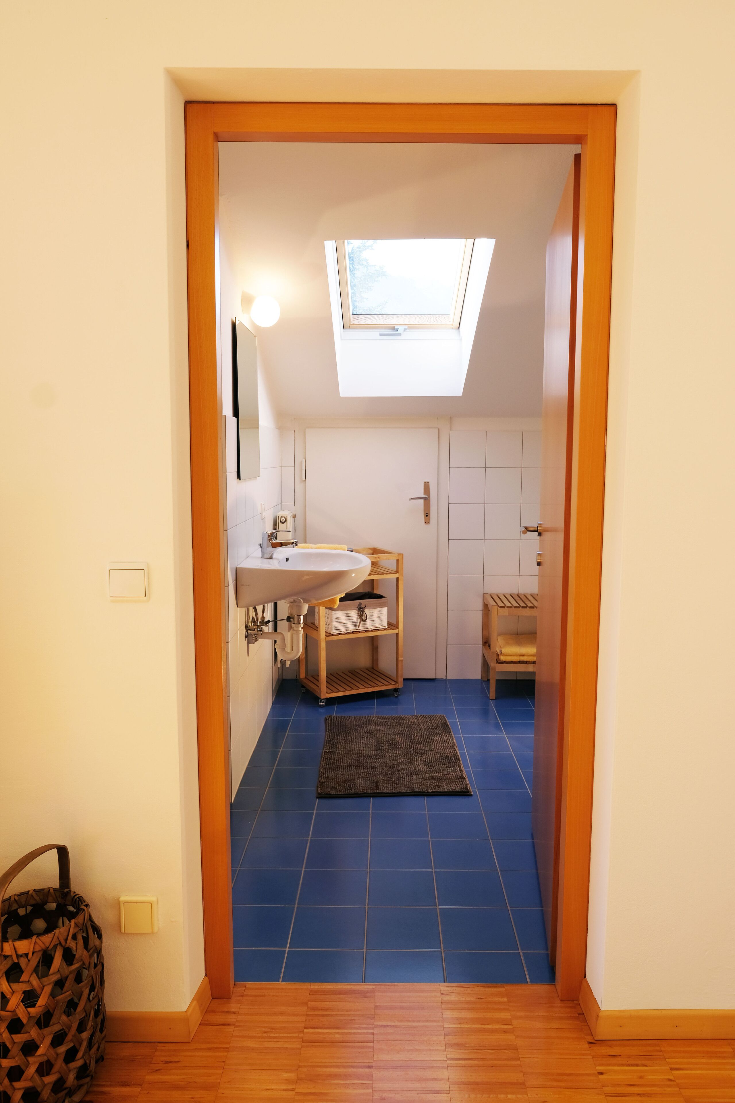 A narrow hallway leading to a bathroom with a skylight, a wooden bench, and a blue-tiled floor.