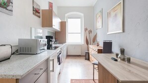 A modern kitchen with a microwave, coffee maker, and wooden cabinets. There is a window providing natural light and a view of the outside. - Apartment Elbflorenz (Dresden)
