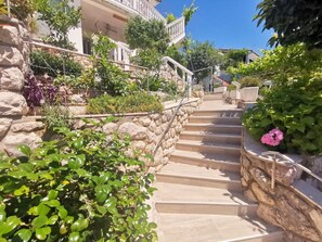 Staircase leads to a second-floor landing with lush greenery and a balcony overlooking the surroundings.