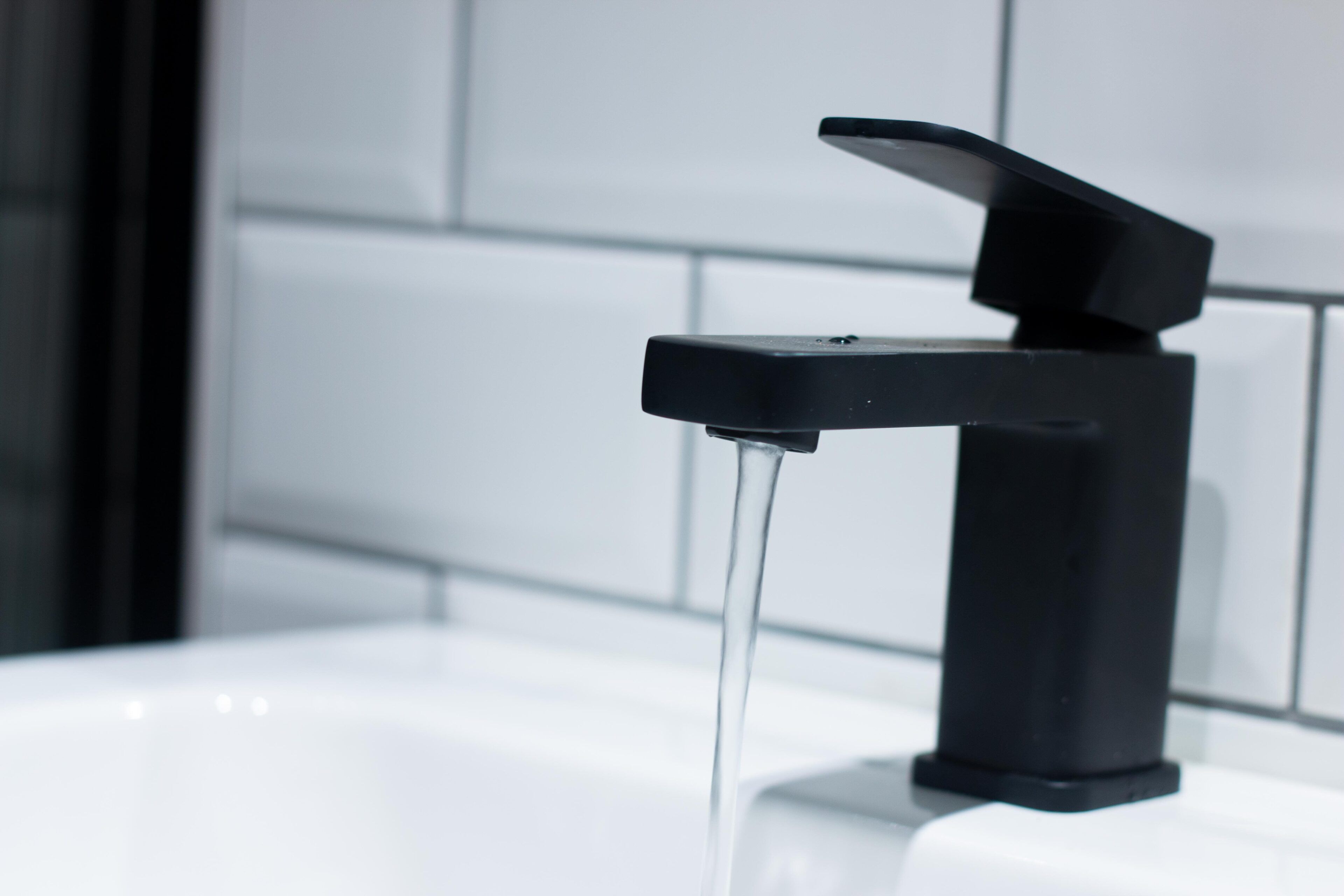 A modern bathroom with a black faucet and clear running water.