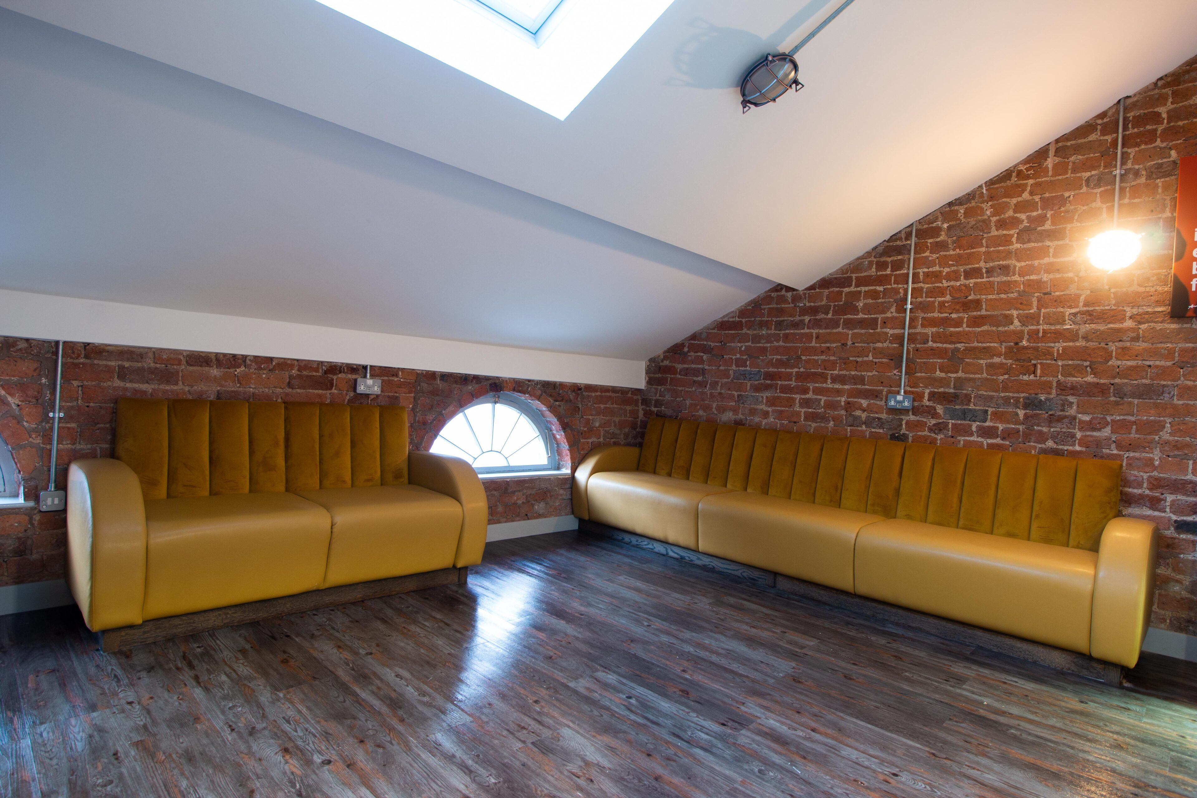 Ein Loft-Zimmer mit Ziegelwand, Holzboden und einem gelben Sofagarnitur.