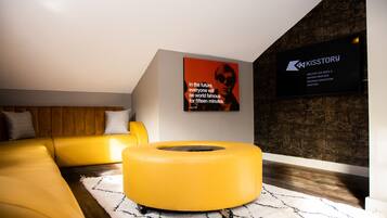 Un salon moderne avec un canapé jaune, un pouf rond jaune et une affiche accrochée au mur.