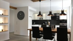 Une cuisine moderne avec des luminaires suspendus, une table à manger avec des chaises et une horloge murale.