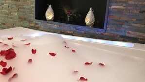 Une baignoire remplie de pétales de rose, une étagère ornée d’objets décoratifs et un mur en briques.