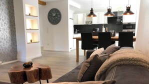 Un salon moderne avec un canapé gris, des tables d’appoint en bois et des luminaires suspendus.