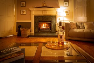 Una sala de estar acogedora con chimenea, un sofá, una mesa de centro de vidrio con una botella y vasos, y una estantería.