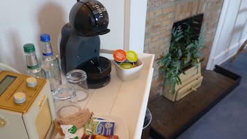 A kitchenette with a coffee maker, bottles, glasses, and snacks.