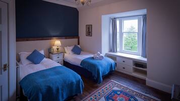 A bedroom with two beds, a window with curtains, a patterned rug, and a chandelier.
