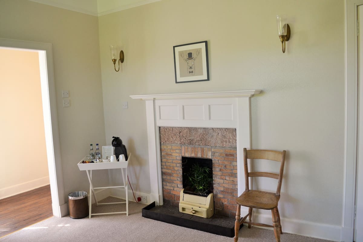 A room with a fireplace, a chair, a small table with bottles, and a trash can.