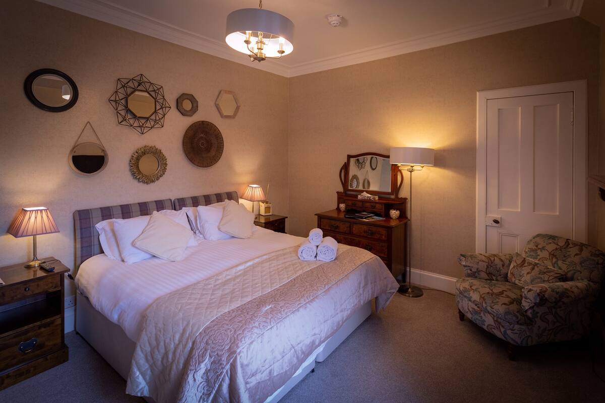 A neatly arranged bedroom with a bed, bedside lamps, a dresser, a chair, and wall decorations.