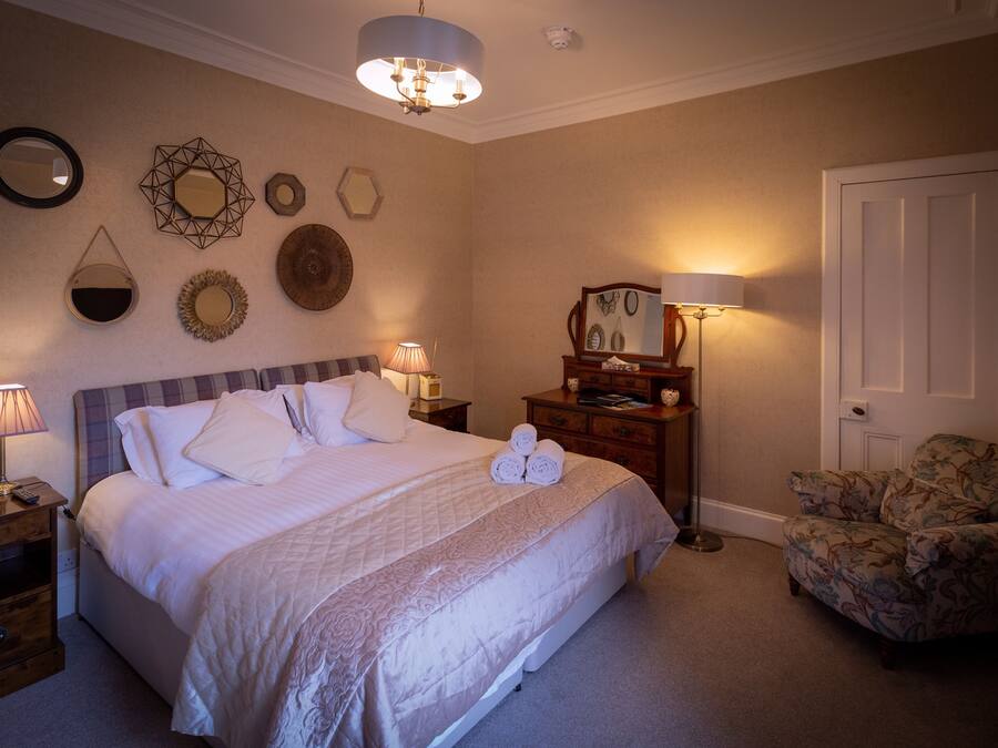 A neatly arranged bedroom with a bed, bedside lamps, a dresser, a chair, and wall decorations.