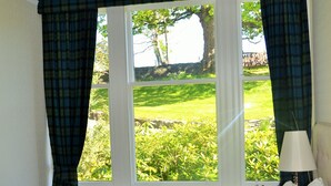 A hotel room with a large bed, plaid curtains, a view of a green landscape, and a lamp on the nightstand. - Craigellachie Lodge (Aberlour)
