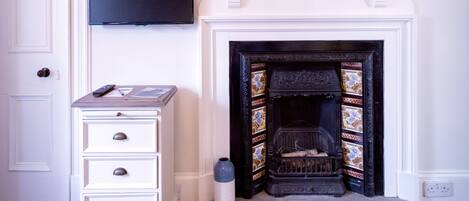 A room with a fireplace, a television mounted above it, a white dresser with drawers, and a patterned rug on the floor.