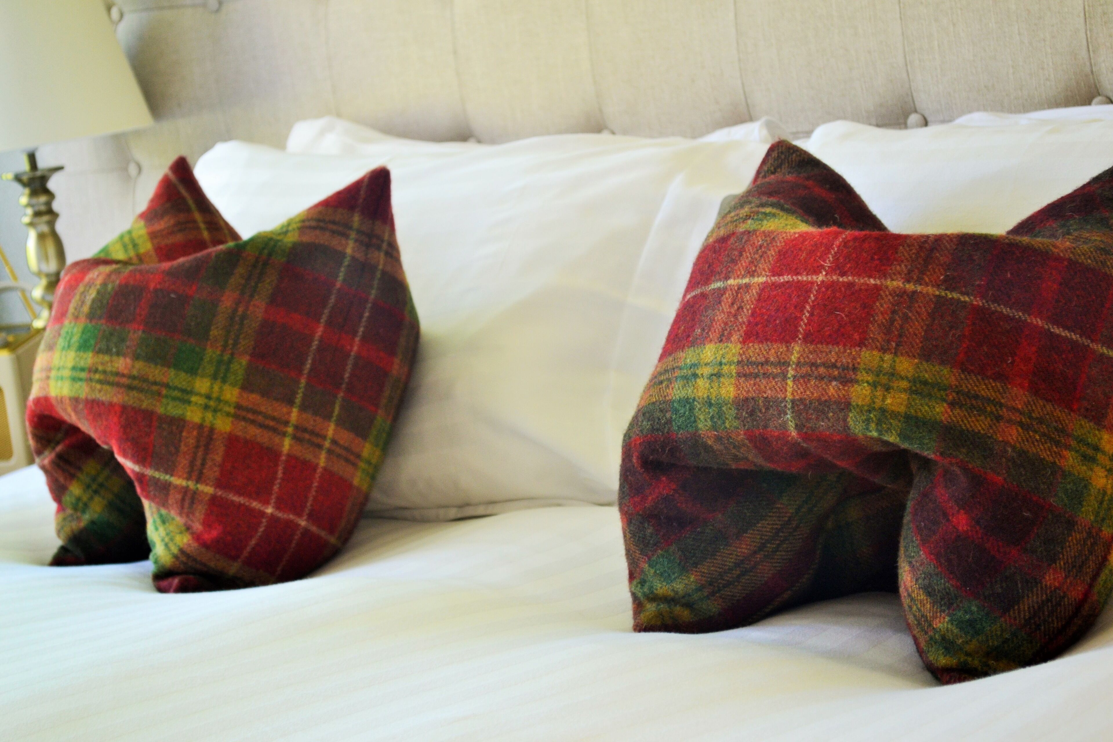 Una cama con sábanas blancas y dos almohadas escocesas.
