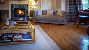 A living room with a fireplace, a sofa, a coffee table with books, and a dining area with a chair. - Craigellachie Lodge (Aberlour)