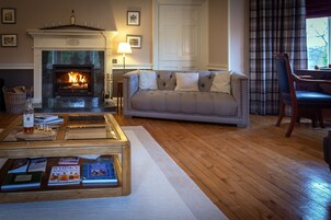 Una sala de estar con chimenea, un sofá, una mesa de centro con libros y una zona de comedor con una silla.