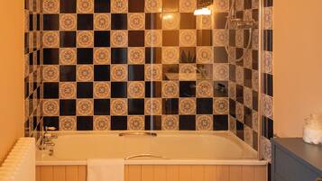 A bathroom with a checkered tile wall, a bathtub, a toilet, and a wooden floor.