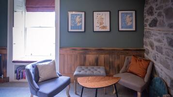 Una sala de estar acogedora con pared azul, paneles de madera y tres mapas enmarcados de Escocia.
