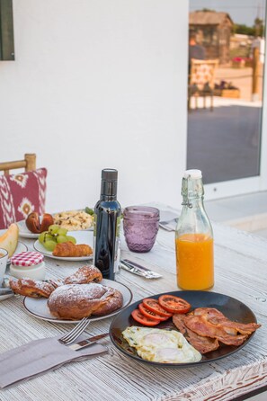 Une table de petit-déjeuner avec des croissants, des œufs, des tomates et une bouteille de jus d’orange.