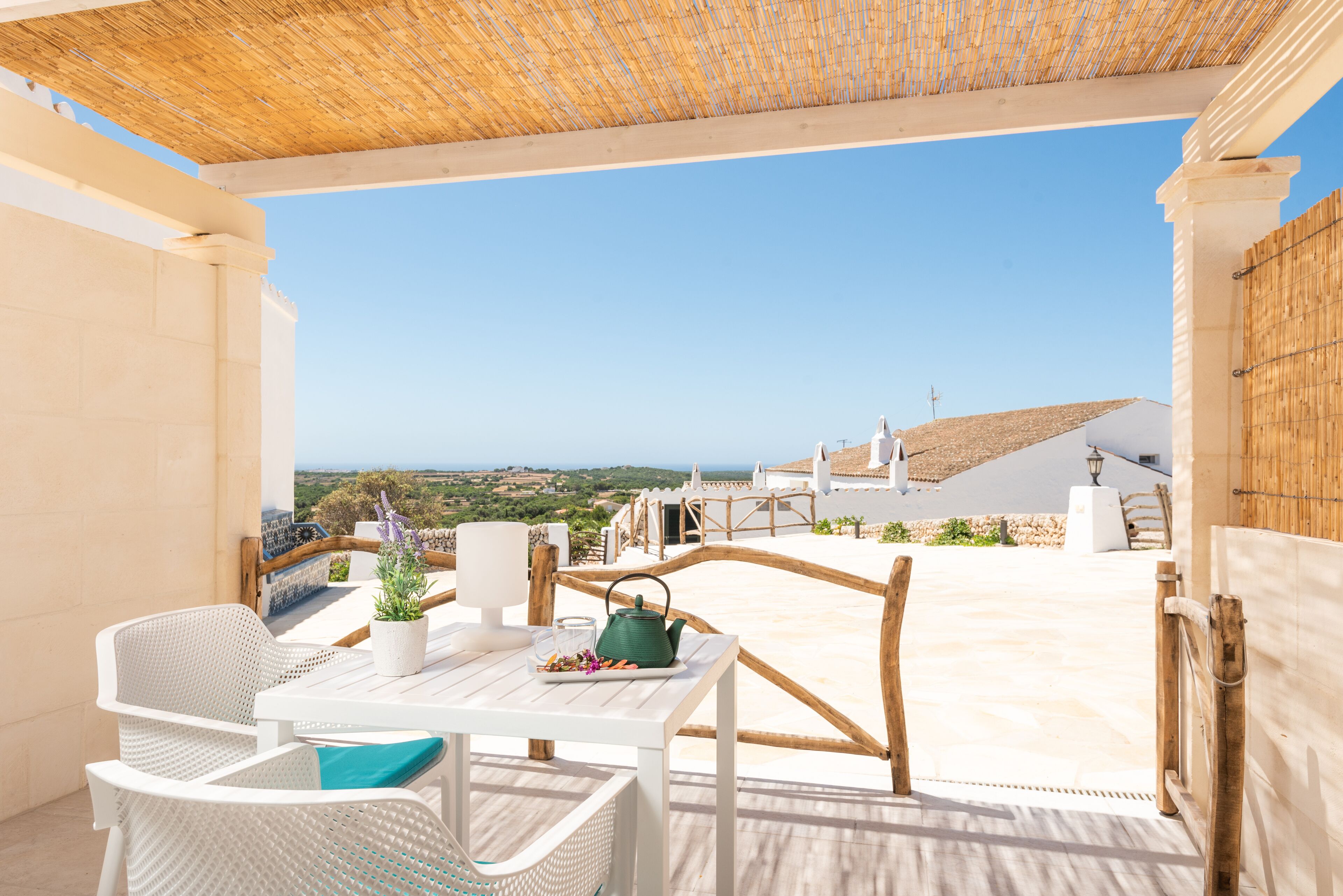 Una terrazza con mobili in vimini bianco, un tavolo con un vassoio di oggetti e vista sul paesaggio.