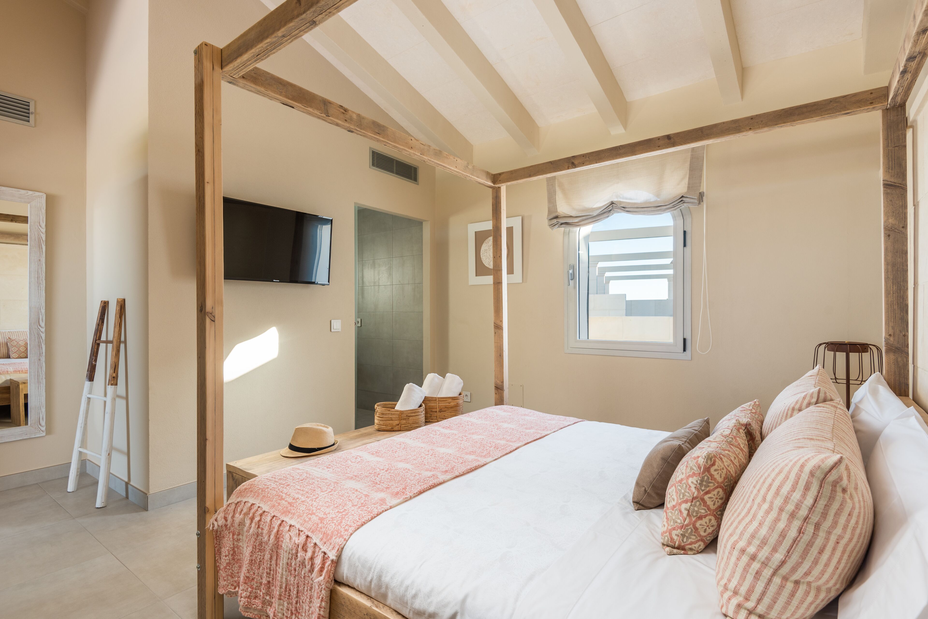 A bedroom with a large bed, wooden beams, a television, a window, and a mirror.