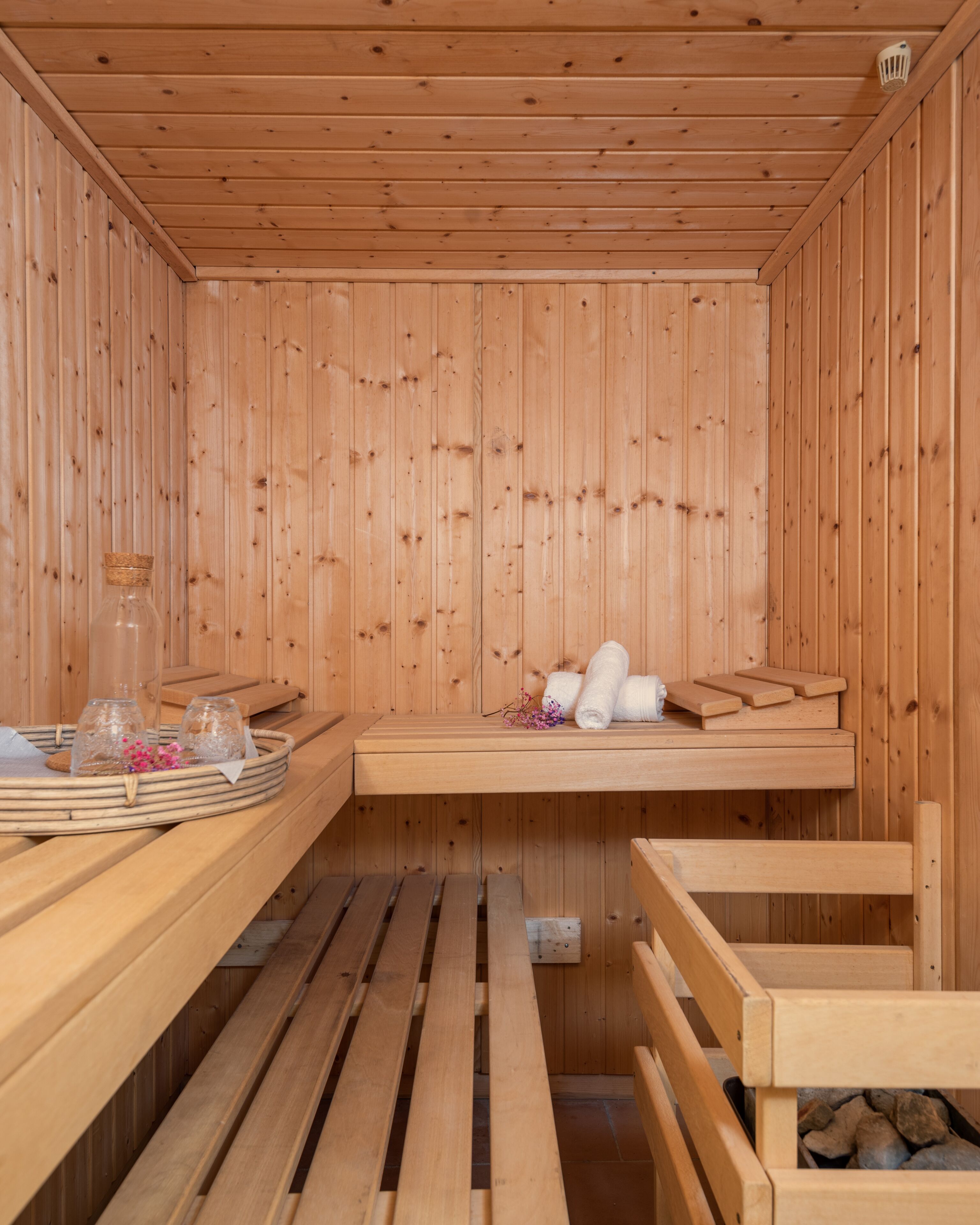 Una sauna de madera con bancos, un banco con toallas y una bandeja con copas y flores.