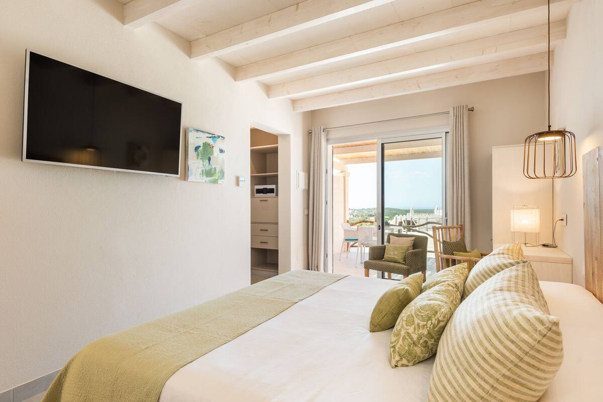 Ein Hotelzimmer mit Bett, Wandfernseher, Balkon mit Aussicht und Schreibtisch mit Stuhl.