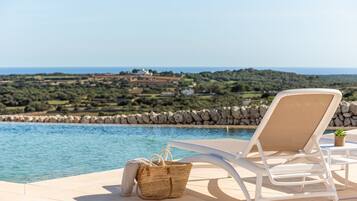 A poolside area with a lounge chair, a wicker basket, and a view of a coastal landscape.