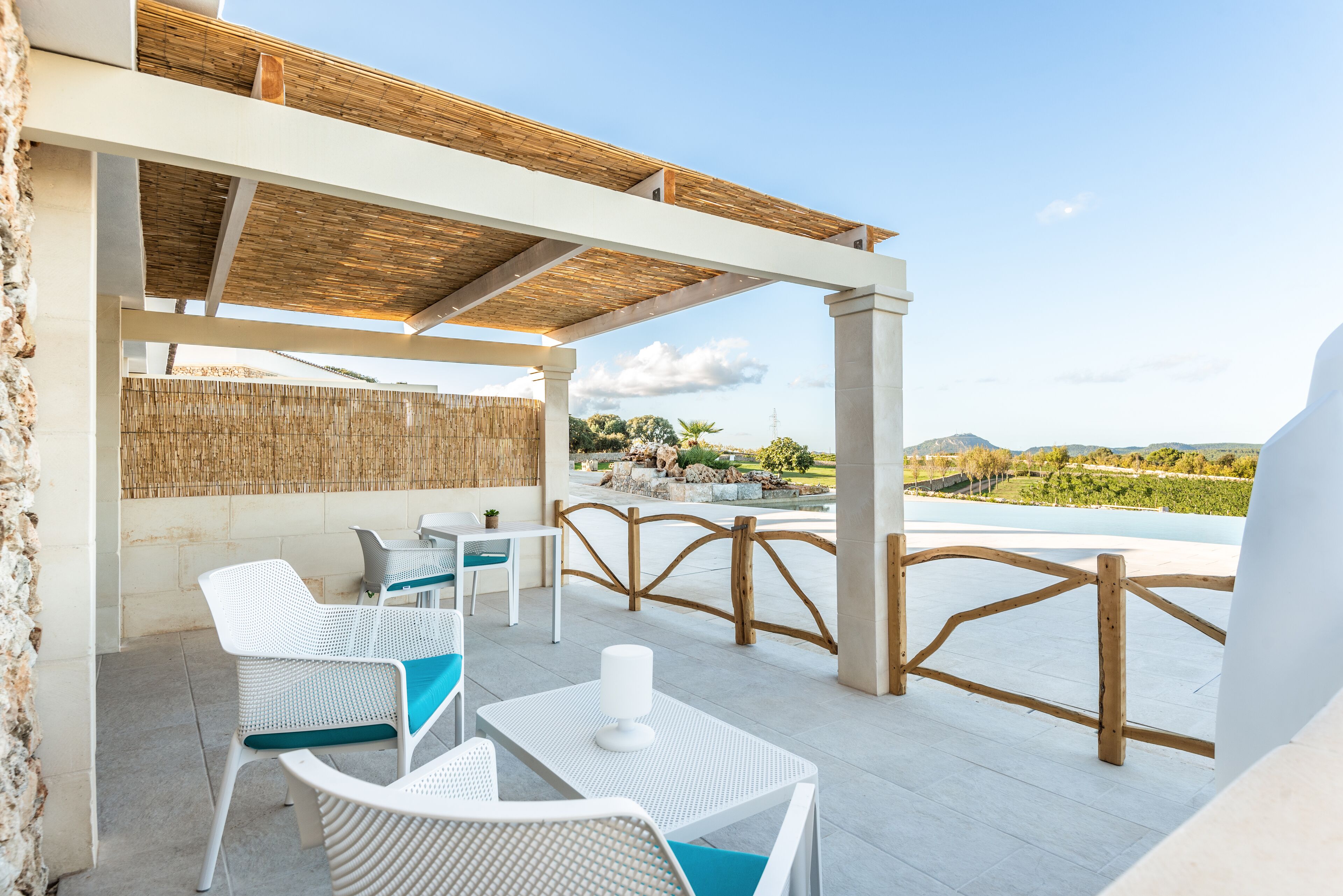 Un patio al aire libre con mobiliario de mimbre blanco, una pérgola de madera y vistas a un viñedo.