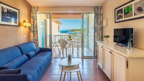 Una sala de estar acogedora con un sofá, una mesita y un televisor. Hay un balcón con vistas al mar.