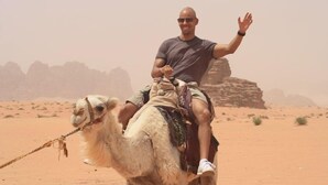 A person riding a camel in a desert with rock formations in the background. - Al sultan bedouin camp (Wadi Rum)