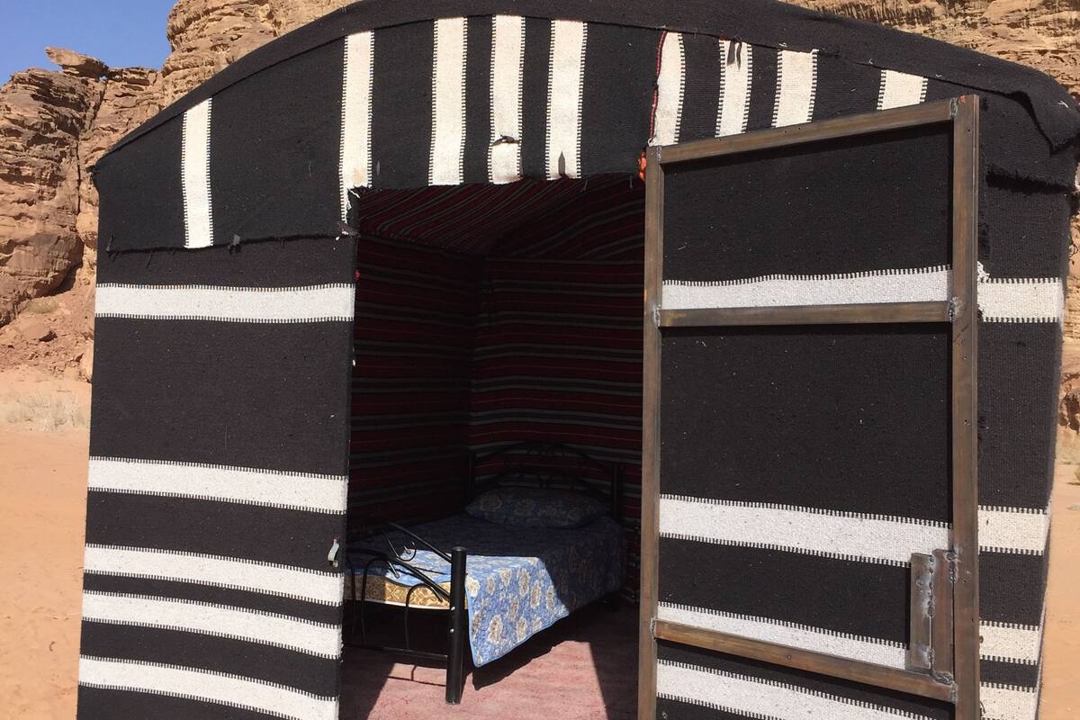 Une petite structure fermée, semblable à une tente, avec un lit à l’intérieur, située devant un paysage désertique rocheux.